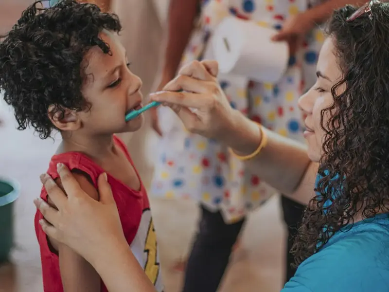 A woman brushing a young boy's teeth while steadying his shoulder