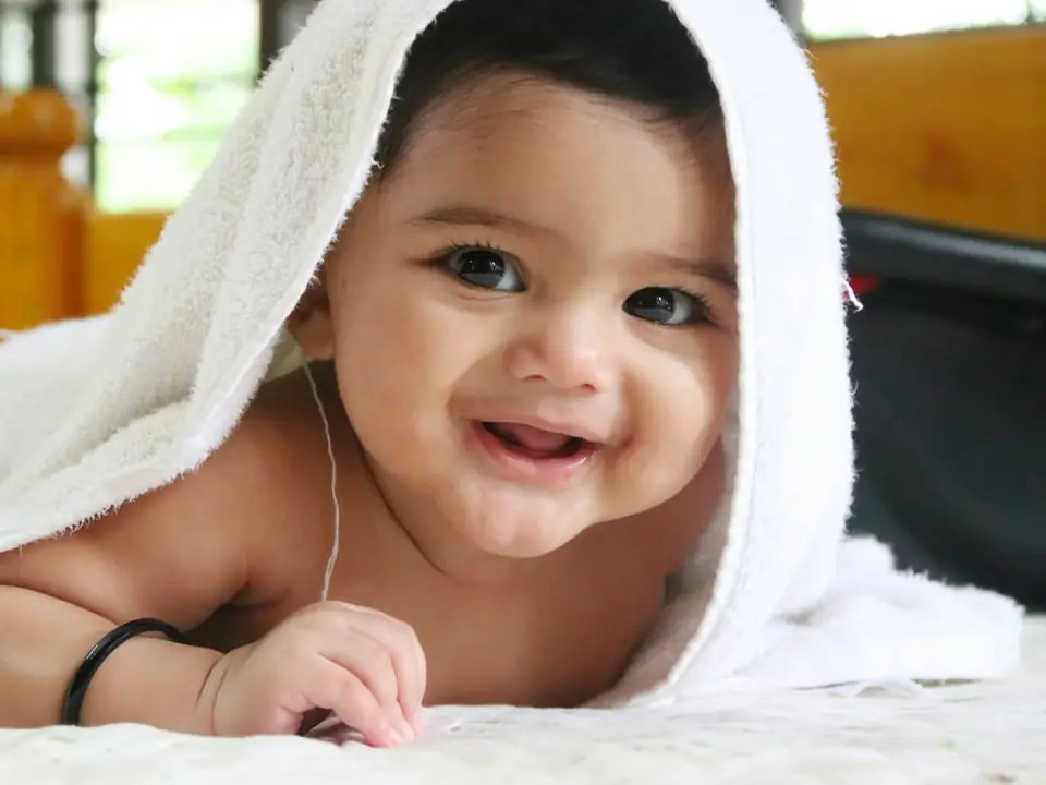 A smiling baby peeking out from under a white towel